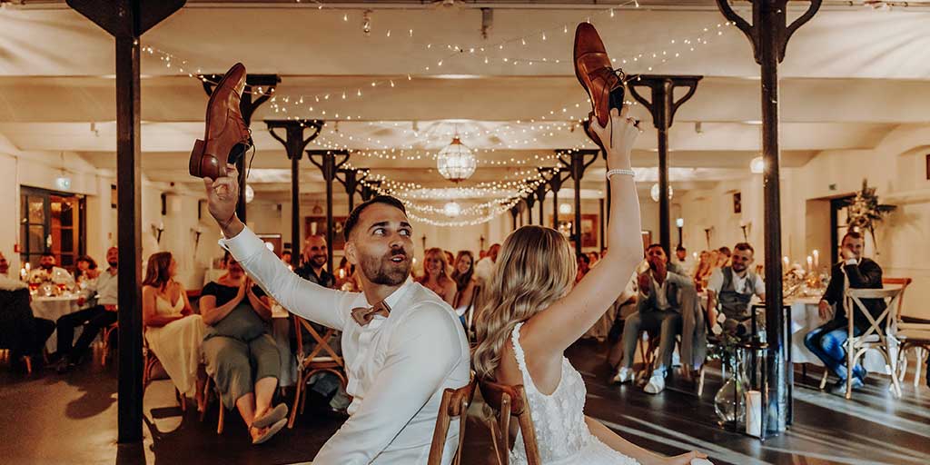 Hochzeitspaar, dass ein Hochzeits-Spiel spielt, bei dem Fragen beantwortet werden müssen indem man den Schuh von Braut oder Bräutigam hochhebt