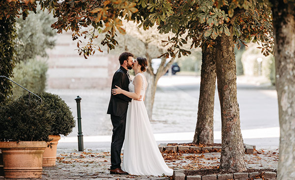 Hochzeitspaar küsst sich unter herbstlichem Baum